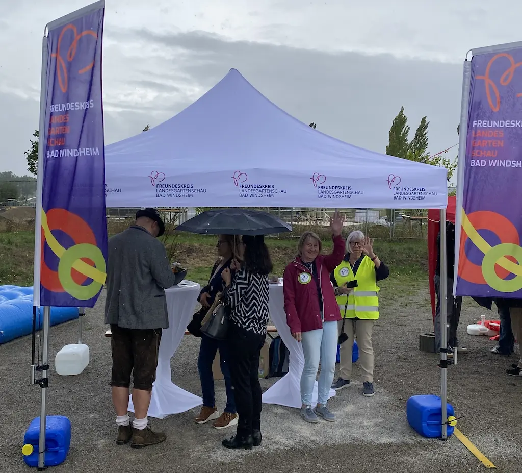 Pavillon des Freundeskreises Landesgartenschau Bad Windsheim mit mehreren Personen und bunten Fahnen auf einem Veranstaltungsgelände.